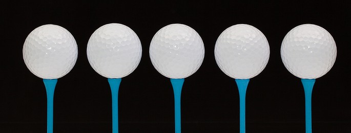 Five Golf Balls on Blue Tees