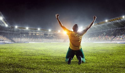 Footballer Celebrating on Knees In Front of Stands