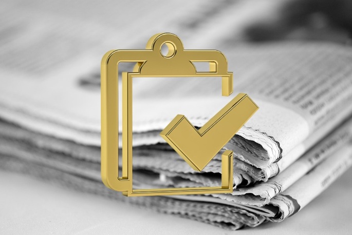 Gold Checklist Against Blurred Stack of Newspapers