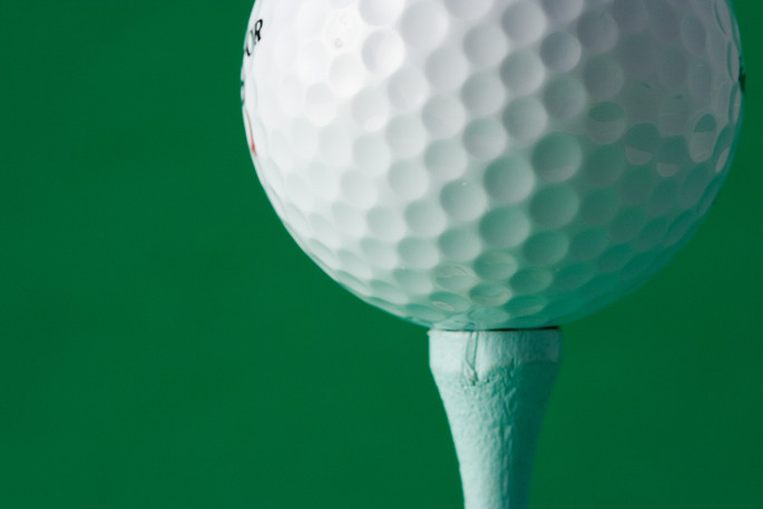 Golf Ball on Tee Against Green Background