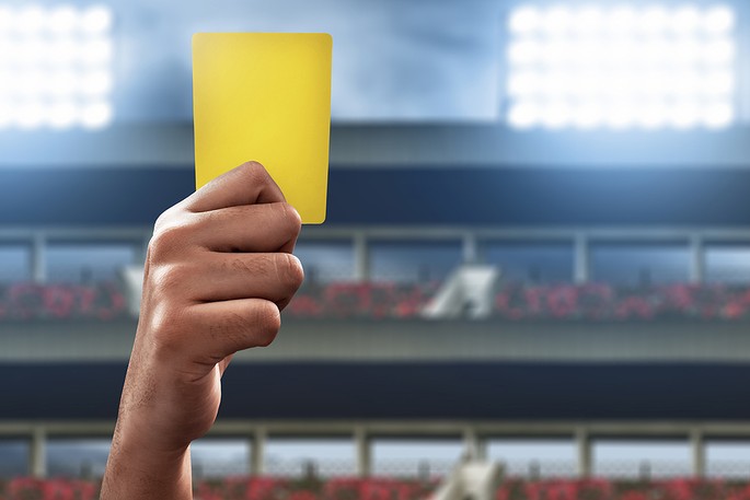 Referee Holding Yellow Card Against Floodlights